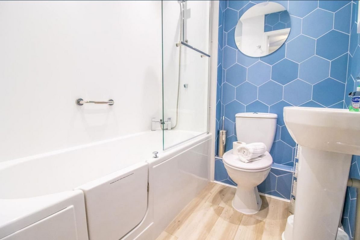 Family bathroom at Beachside Cottage with blue hexagon tiles, bath with overhead shower, basin and WC