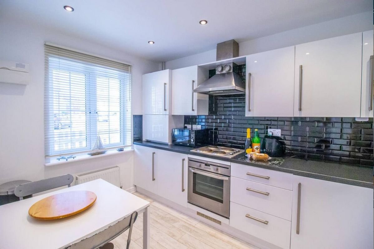 Modern white kitchen at Beachside Cottage with breakfast table, oven and dark tiled splashback